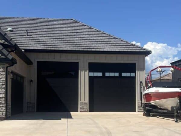 Modern home with two black garage doors and a boat parked nearby.